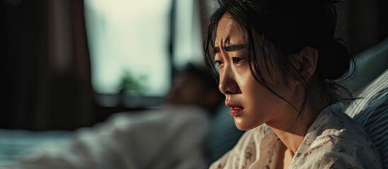 Unhappy stressful Asian woman sitting and crying on the bed while her husband sleeping a family and post marriage problem Arguing Asian young couple with bad negative relationship. Copy space image - Powered by Adobe