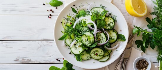 Crunchy cucumber onion salad with fresh dill mint leaves with lemon on a white plate with a fork with ceramic shakers with salt pepper toothpicks on a white wooden table close up. Copy space image - obrazy, fototapety, plakaty
