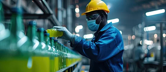 Foto op Plexiglas African male factory worker wearing medical mask picking up green juice bottle or basil seed drink for checking quality in beverage factory. Copy space image. Place for adding text © Ilgun