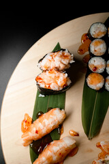 Top view closeup of part of a set of sushi rolls with fillings, covered in sauce and nigiri decorated with banana leaves