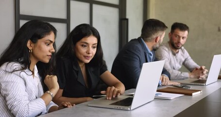 Two friendly young multiethnic female coworkers teammates working on joint project in coworking space with diverse colleagues, look laptop at screen, share opinion, creative ideas engaged in teamwork - Powered by Adobe