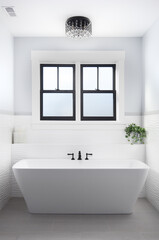 A beautiful, luxury bathroom with a light hanging above a white standalone tub and black faucet...