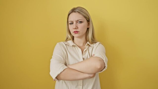 Nervous young blonde woman showing skeptic, disapproving expression, crossed arms negative person. standing isolated against yellow background.