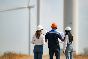 Back view of group engineers walking and looking at wind turbines in a windmill farm.