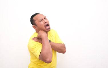 PORTRAIT OF THE EXPRESSION OF AN ASIAN MAN IN YELLOW T-shirt FEELING PAIN IN THE SHOULDER