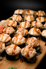 Top view of three portions of baked sushi rolls with unagi sauce, sesame seeds, wasabi, red and white ginger
