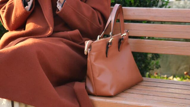  women with stylish casual purse sitting on park bench 