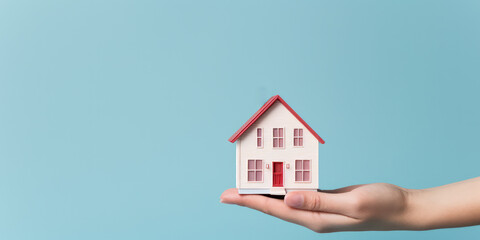 Hand holding a cartoon house model against a serene blue background. Home buying concept. Generative AI