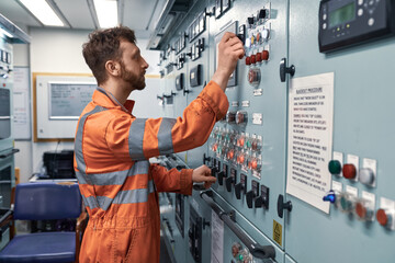 Young engineer working in engine control room on electrical distribution system to synchronize work...