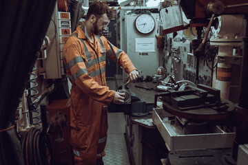 Young mechanical engineer repairing engine part, secured in vice in workshop, wearing coverall and goggles.