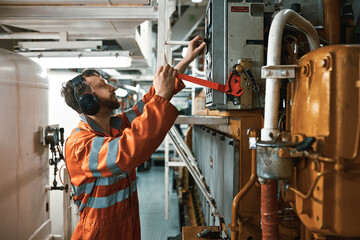 Young engineer officer in engine room, wearing personal protective equipment, starting main diesel engine manually.