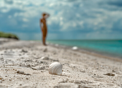 young nude girl walks on an empty beach near the sea surf against the blue sky with clouds in summer