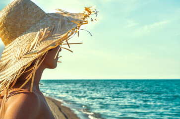 young girl in a straw hat on the background of the surf of the sea and sky with clouds closeup