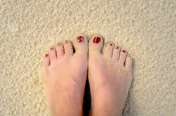 female legs with a red pedicure on the sand on the beach closeup