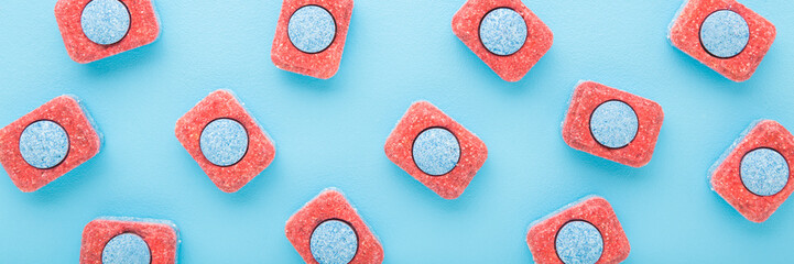 Red blue dishwasher tablets on light blue table. Wide banner. Pastel color. Closeup. Top down view.