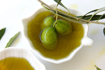 Extra virgin olive oil in a white plate with a branch of olives and leaves on a white background with drops of olive oil. Plate with olive oil and olive. Healthly food.