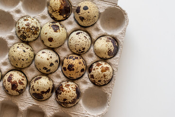 Spotted quail eggs in an egg box on a yellow background, natural eco friendly products.