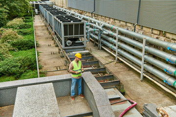 good looking technician in helmet and safety vest holding clipboard while outside, data center