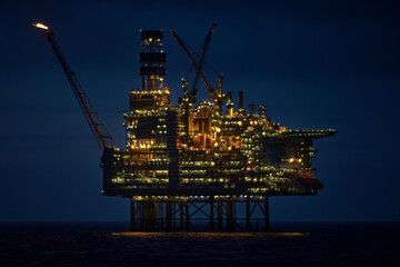 Close up view of illuminated drilling rig at night, with dark blue sky in the deep blue ocean.