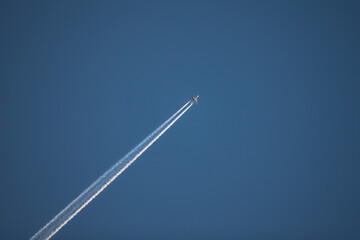 Photo of airplane flying diagonally in the clear blue sky, leaving vapor trail in the air.