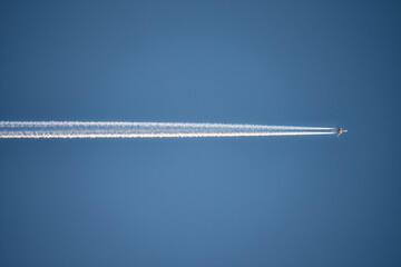 Photo of airplane flying horizontally  in the clear blue sky, leaving vapor trail in the air.
