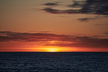 Dramatic colourful dark sky in the sea with waves on the water and sun on the horizon.