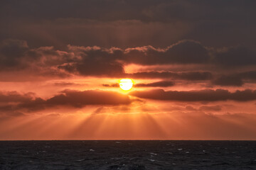 Beautiful red and yellow sunset in the sea with sun in the sky and sun rays shining through the...