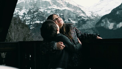 Younger brother kissing sister ont he cheek standing in Swiss chalet balcony during winter season...