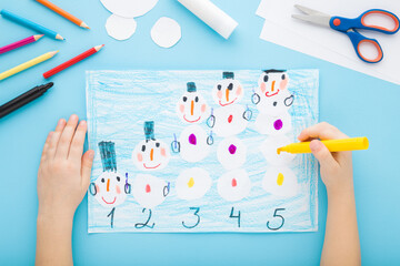 Little child hands creating and decorating snowman shapes and learning numbers on paper on light...