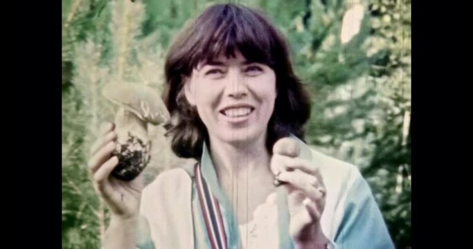 Beautiful woman hold mushrooms in hands, close up. Happy woman portrait on green forest background. Female mushroom picker rejoice in harvest hobby. Vintage color film. Family archive. Retro 1980s