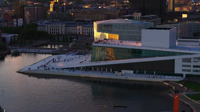 Aerial view of people walking on promenade and lookout platform at modern Oslo Opera House on waterfront at sunset. Oslo, Norway