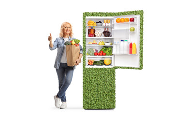 Woman with a grocery bag leaning on an green efficient fridge and gesturing thumbs up