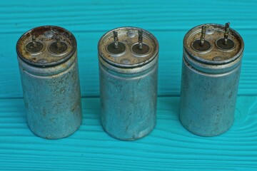 three old electrolytic round aluminum dirty powerful large capacitors stand on a green wooden table
