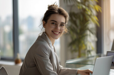 A cheerful professional woman with glasses typing on her laptop, office buildings in the background