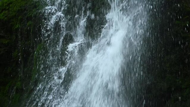 Water falls on and sprinles from mossy stones from a waterfall (slow motion)