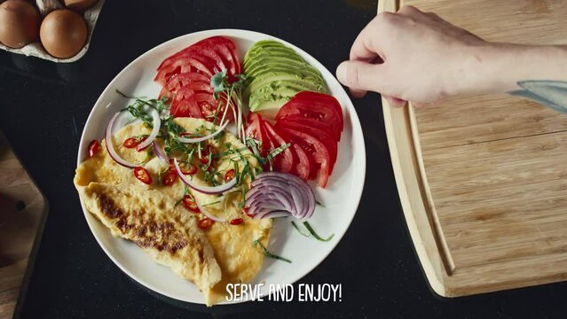 Top down shot of hand of chef serving omelet with vegetables and herbs on plate, subtitles appearing below screen during video recipeTop down shot of hand of chef serving omelet with vegetables and he
