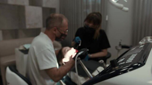 Two doctors, a man and a woman in protective masks in a dental clinic, serve a patient. The work of an orthodontist. The concept of healthcare and medicine.