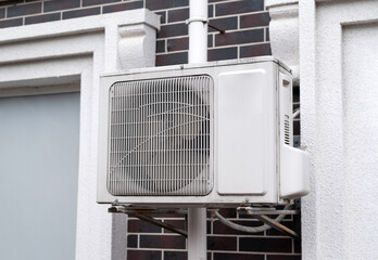 Outdoor air conditioning unit mounted on a building wall, with visible pipes and metal support...