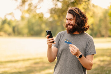 Bearded man with long hair buys something online on the phone using credit card.