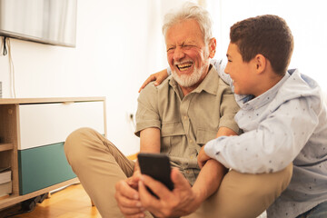 Grandfather and grandson using mobile phone at home