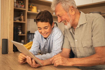 Smiling grandfather and grandson using tablet together at home