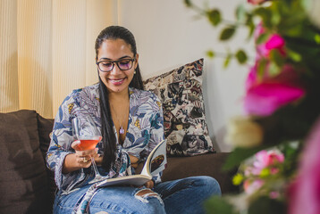 joven mujer lee un libro en la sala de la casa y con una copa de vino en la mano