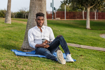 Obraz premium African-American man sitting under a tree using a cell phone
