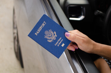 In a car, a hand holds a closed American passport, anticipating travels and discoveries.