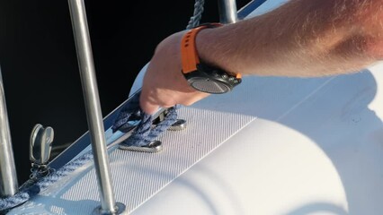 Man sailor removes mooring ropes from cleat to start sailing. Yachtsman unties knot on mooring cleat preparing sailboat to move