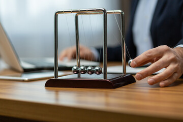 Mature businessman in a suit interacts with a Newton's cradle on his desk, symbolizing decision...