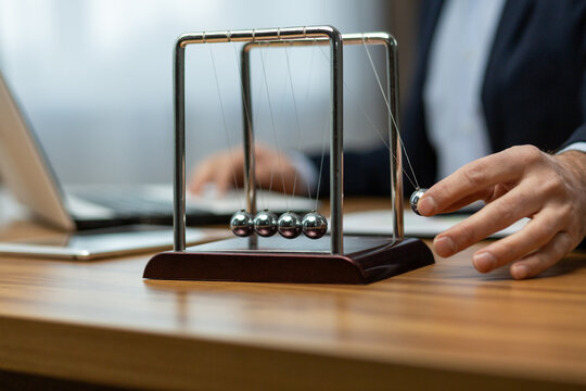 Mature businessman in a suit interacts with a Newton's cradle on his desk, symbolizing decision making and focus.