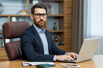 Focused mature man in stylish office working on laptop. Business professional, lawyer, or banker in a home environment. - obrazy, fototapety, plakaty