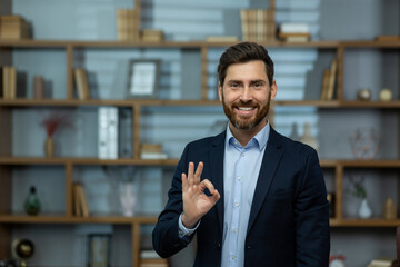 Professional mature male business owner showing positive approval with an okay hand sign in a...