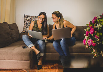 pareja de mujeres ejecutivas trabajando en la casa sentadas en el sofá y con sus computadoras   - obrazy, fototapety, plakaty